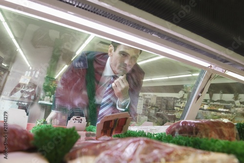 Photo: Mature man looks through glass of meat counter in supermarket Mature man looks through glass of meat counter in supermarket