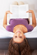 Silly girl holding a book while upside down on bed Silly girl holding a book while upside down on bed
