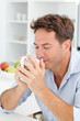 Handsome man smelling his coffee sitting in his kitchen Handsome man smelling his coffee sitting in his kitchen