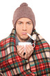Ill man covered with blanket holding a tea cup