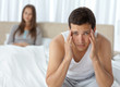 Photo: Tired man having a headache sitting on the bed with his girlfrie Tired man having a headache sitting on the bed with his girlfrie