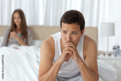 Photo: Pensive man having a headache sitting on the bed Pensive man having a headache sitting on the bed