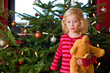 girl with teddy in front of christmas tree