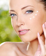 Beautiful woman applying cream near eyes