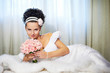 Foto: Beautiful bride with bouquet of flowers on white bed Beautiful bride with bouquet of flowers on white bed
