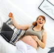 Laughing beautiful pregnant woman with laptop and credit card.