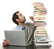 uomo con pila di libri e computer seduto ad un tavolo