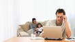 Angry man on his laptop while his family is on a sofa