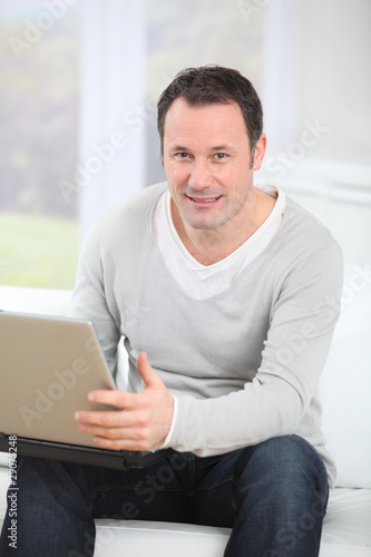 Photo: Man sitting in couch using laptop computer Man sitting in couch using laptop computer
