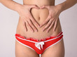 A woman's hands forming a heart symbol around navel