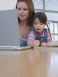 Mother Using Laptop While Daughter Colors