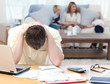 Man calculating his bills while his family are on the sofa Man calculating his bills while his family are on the sofa