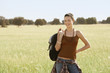 Female hiker holding backpack, standing in field, portrait