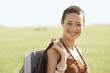 Female hiker holding backpack, standing in field, portrait