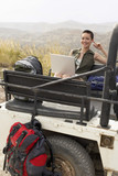 Photo: Woman using laptop sitting in back of four wheel drive car, in desert, portrait Woman using laptop sitting in back of four wheel drive car, in desert, portrait