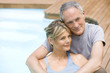 Middle-aged couple sitting embracing by swimming pool, portrait