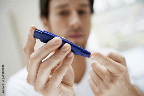 Photo: Man using lancelet on finger in bathroom, close up Man using lancelet on finger in bathroom, close up