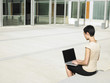 Foto: Young woman sitting in plaza courtyard using laptop Young woman sitting in plaza courtyard using laptop