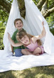 Young boy and girl in backyard sitting in tent made of bed sheet