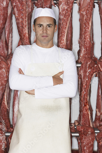 Photo: Butcher Standing, arms crossed, in front of raw meat in Meat Locker Butcher Standing, arms crossed, in front of raw meat in Meat Locker