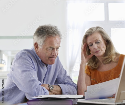 Photo: Senior couple looking at bills, sitting at dining table Senior couple looking at bills, sitting at dining table