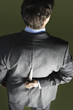 Mid-adult businessman standing, holding knife behind back, back view