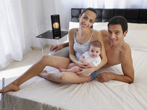 Photo: Couple laying on a bed with baby daughter Couple laying on a bed with baby daughter