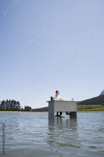 Photo: Businesswoman sitting at desk in water with laptop Businesswoman sitting at desk in water with laptop