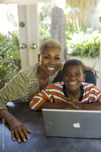 Photo: Woman and young boy at a table with laptop smiling Woman and young boy at a table with laptop smiling