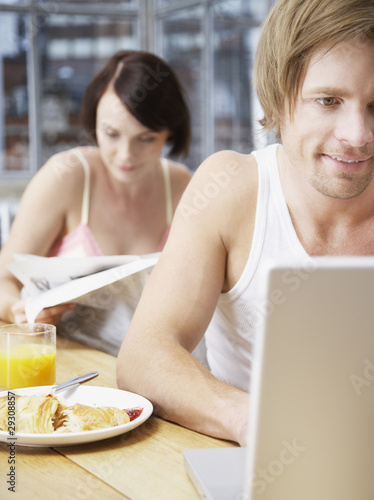 Photo: Couple in a kitchen with the woman reading and the man on a laptop Couple in a kitchen with the woman reading and the man on a laptop
