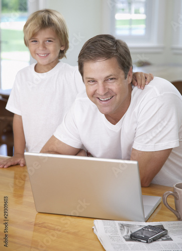 Photo: Man and young boy in kitchen with laptop Man and young boy in kitchen with laptop