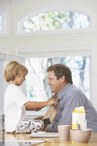 Photo: Young boy tying man's necktie in kitchen Young boy tying man's necktie in kitchen