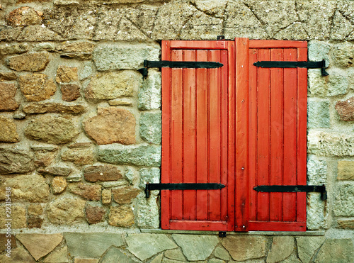Photo: Red shutter window in many textured stone wall Red shutter window in many textured stone wall