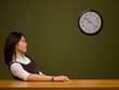 An asian woman sitting at a desk watching the clock An asian woman sitting at a desk watching the clock