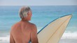 Mature man looking at the ocean with a surfboard