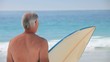 Elderly man looking at the ocean with a surfboard