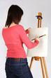 young girl in red shirt standing near easel and painting, back v