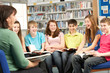 Teenage Students In Library Reading Books With Tutor