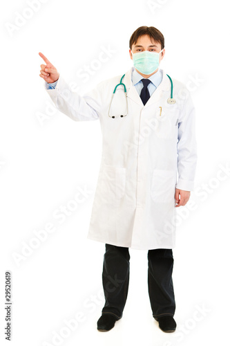 Photo: Medical doctor wearing mask and pointing finger in corner Medical doctor wearing mask and pointing finger in corner