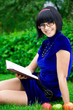 Young beautiful woman lays on green field with apple and book
