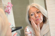 Senior woman applying moisturizer on her face
