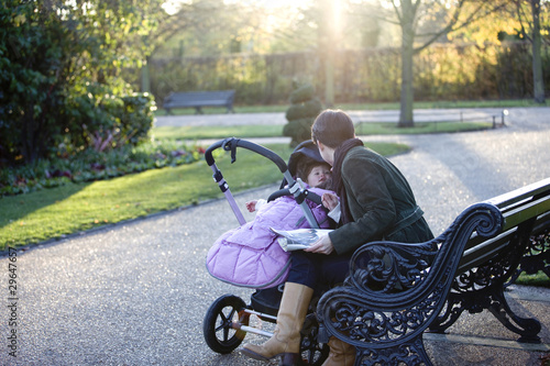 Photo: A mother sitting on a bench, looking at her daughter in a buggy A mother sitting on a bench, looking at her daughter in a buggy