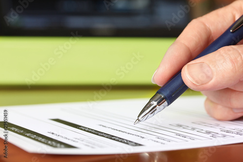 Photo: Hand with Pen Signing Form by Green Folder Hand with Pen Signing Form by Green Folder