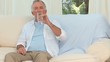 Retired man drinking medicine on his sofa