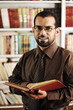 Young man standing in university library reading and smiling Young man standing in university library reading and smiling