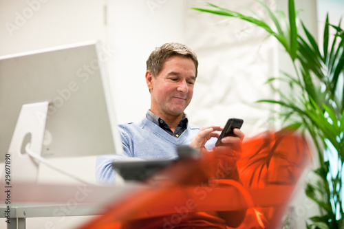 Photo: Businessman text messaging in office Businessman text messaging in office
