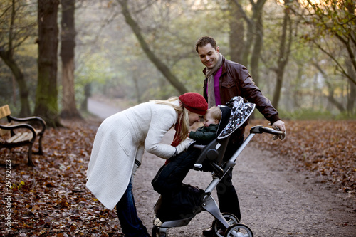 Photo: A young couple standing with a stroller in the park A young couple standing with a stroller in the park