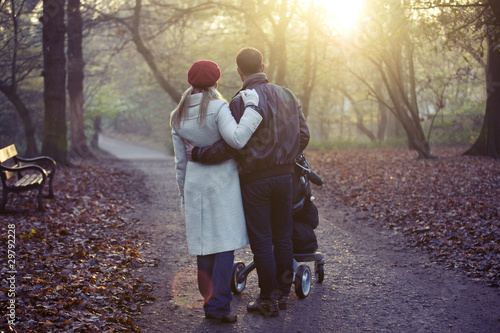 Photo: A young couple pushing a stroller in the park, rear view A young couple pushing a stroller in the park, rear view