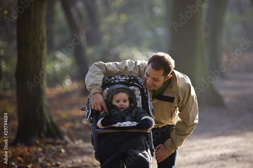 Photo: A young father with his son in a stroller in the park A young father with his son in a stroller in the park