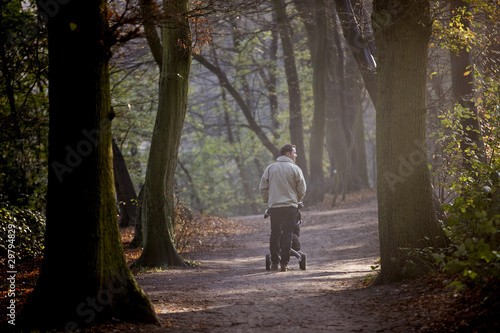 Photo: A young father pushing a stroller in the park, rear view A young father pushing a stroller in the park, rear view